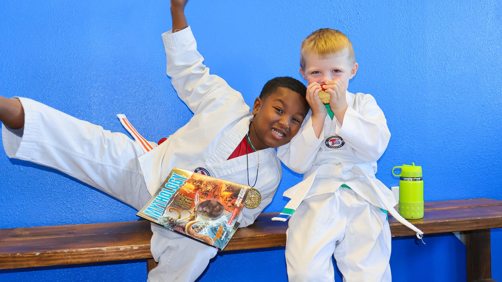 Two young students sitting on a bench after class, one holding a book and a medal