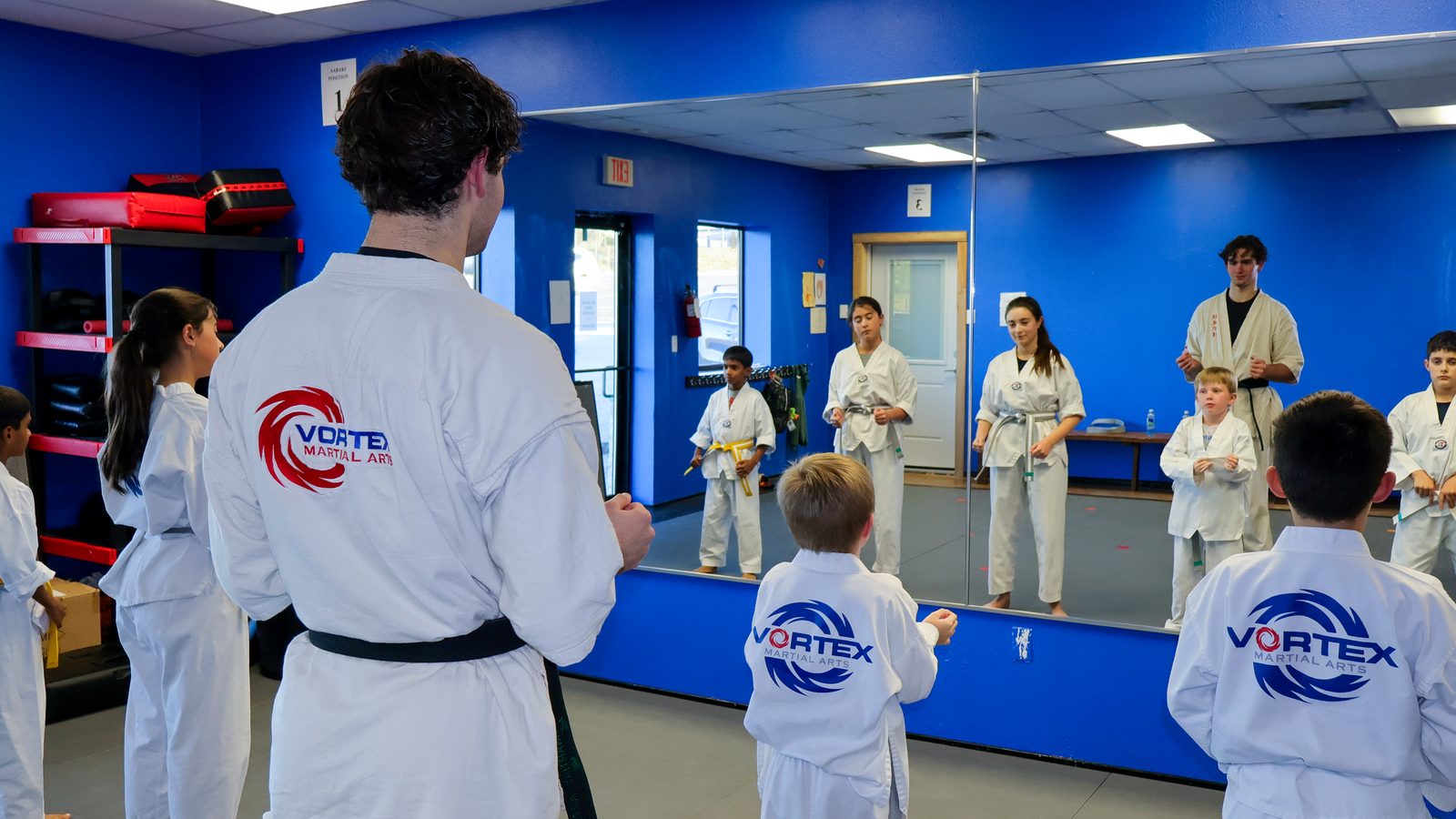 The Vortex training room with a mirrored wall, blue mats and students lined up for class