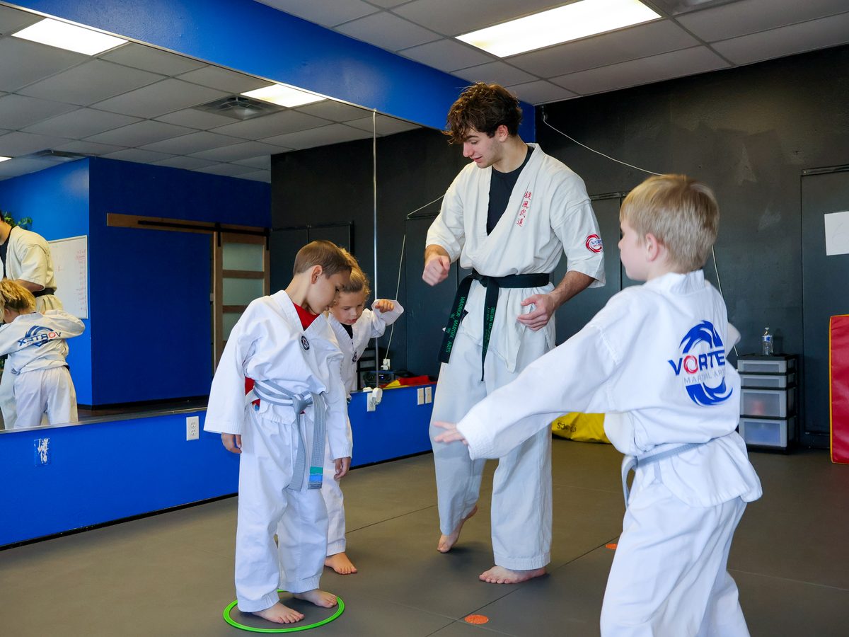 An instructor demonstrating a stance to two young students standing side by side on the mat