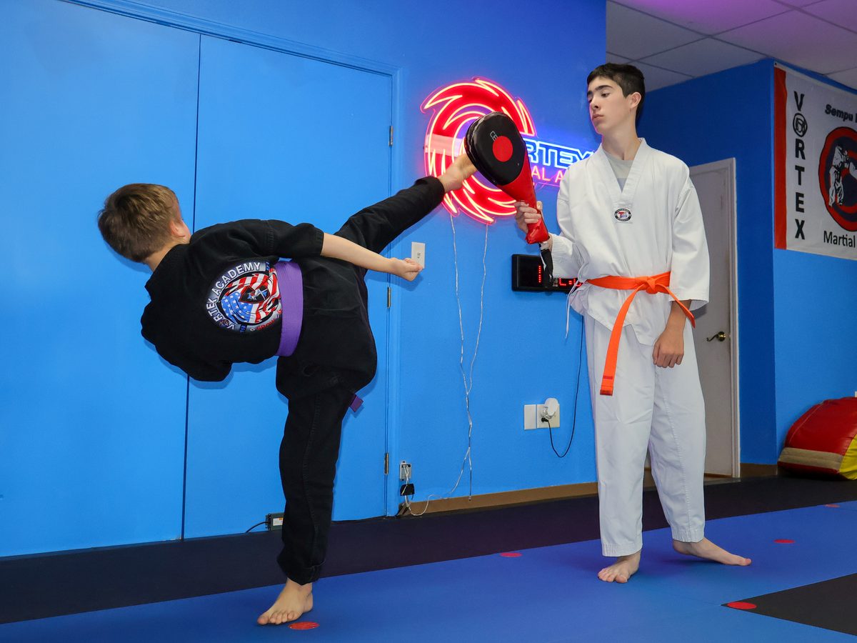 A student throwing a high roundhouse kick into a focus pad held by an instructor